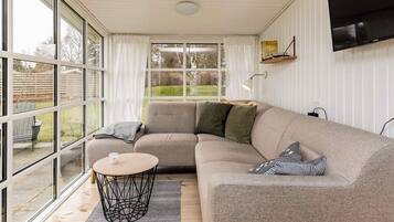A modern living room with a sectional sofa, a round coffee table, and large windows offering a view of the outdoors.