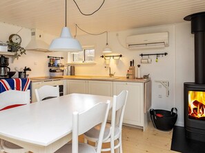 Una cocina moderna con armarios blancos, una mesa de comedor, una lámpara colgante y un estufa de leña.