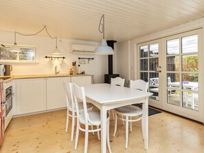 A kitchen with a white table and chairs, an oven, and a window with a view of the outdoors. - 4 Person Holiday Home in Vaeggerlose (Vaeggerlose)