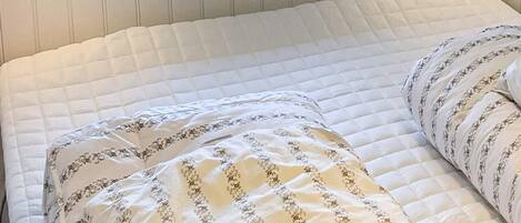 A bed with a quilted white mattress and two pillows with a floral pattern.