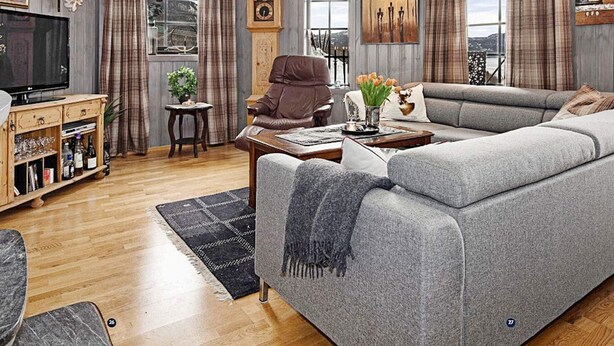 A modern living room with a grey sofa, wooden entertainment unit, and a large window with curtains. - 4 Star Holiday Home in Noresund (Krodsherad)