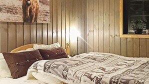 A wooden-paneled room with a bed, pillows, a framed picture of a yak, and a window with a plant. - 4 Star Holiday Home in Noresund (Krodsherad)
