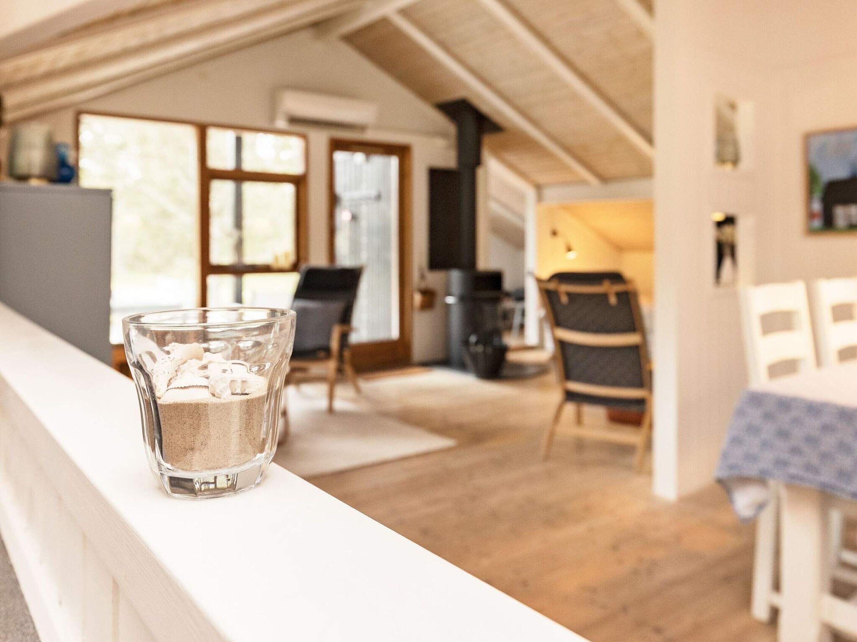 A glass of water on a white counter in a well-lit room with wooden flooring, a dining area, and a kitchen in the background.
