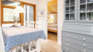 A cozy room with a dining table, chairs, a cabinet with glass doors, and a bed in the background. - 6 Person Holiday Home in Albaek (Aalbaek)