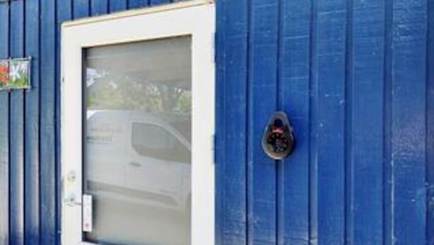 Un edificio blu con una finestra a cornice bianca e una porta, un piccolo cartello e una telecamera di sicurezza.