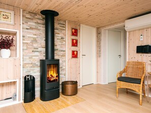 Una sala de estar acogedora con una estufa de leña, un sillón de mimbre y una puerta blanca.