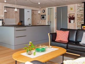 A modern kitchen with a microwave, a refrigerator, and a wooden cabinet. There is a dining area with a table and a sofa. - 4 Star Holiday Home in Ulfborg (Ulfborg)