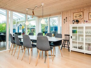 A dining area with a wooden ceiling, large windows, and a white cabinet with glassware.