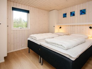 A bedroom with a wooden paneled wall, a window, a bed with white bedding, and a wall-mounted light fixture.