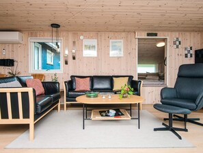 A room with a wooden ceiling, a black leather sofa, a wooden coffee table, and a black armchair.