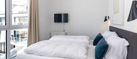 Una habitación de hotel moderna con una cama grande, un televisor de pantalla plana en la pared y vistas de la ciudad a través de amplios ventanales.