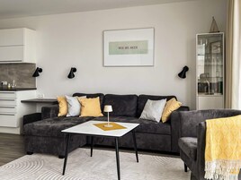 Un salon moderne avec un canapé gris foncé, une petite table blanche et un plaid jaune.