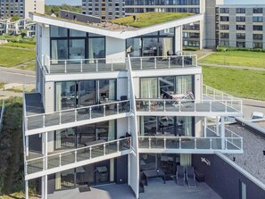 Um edifício moderno de vários andares com varandas de vidro, área de estar externa e um telhado plano com vegetação.