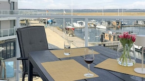 Une table avec un verre de vin rouge et un vase de fleurs, donnant sur une marina avec des bateaux et une plage.