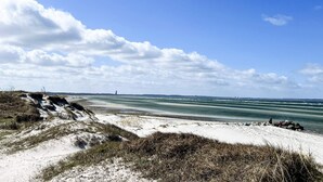 Ein Strand mit Dünen, einem klaren Himmel und einem entfernten Blick auf eine Stadtlinie.