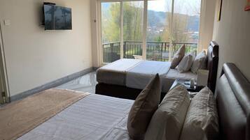 Habitación de hotel con dos camas, televisor y balcón con vista a árboles y edificios.