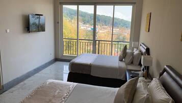 Habitación de hotel con dos camas, un televisor, un balcón con vistas a la ciudad y aire acondicionado instalado.