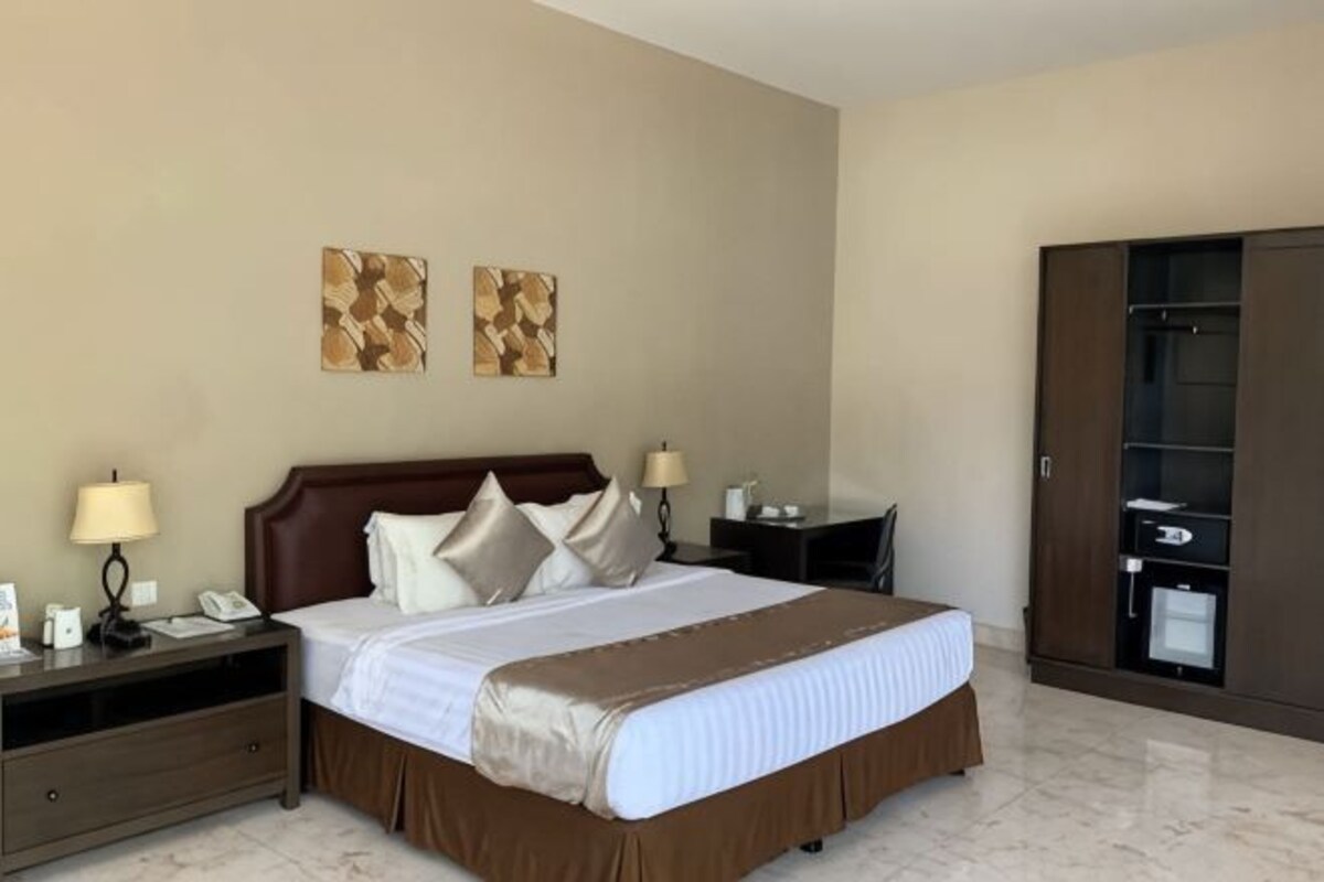 A hotel room with a bed, nightstands, lamps, a wardrobe, and artwork on the wall.