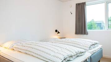 A bedroom with a bed, a bedside lamp, a window with curtains, and a view of the outside.