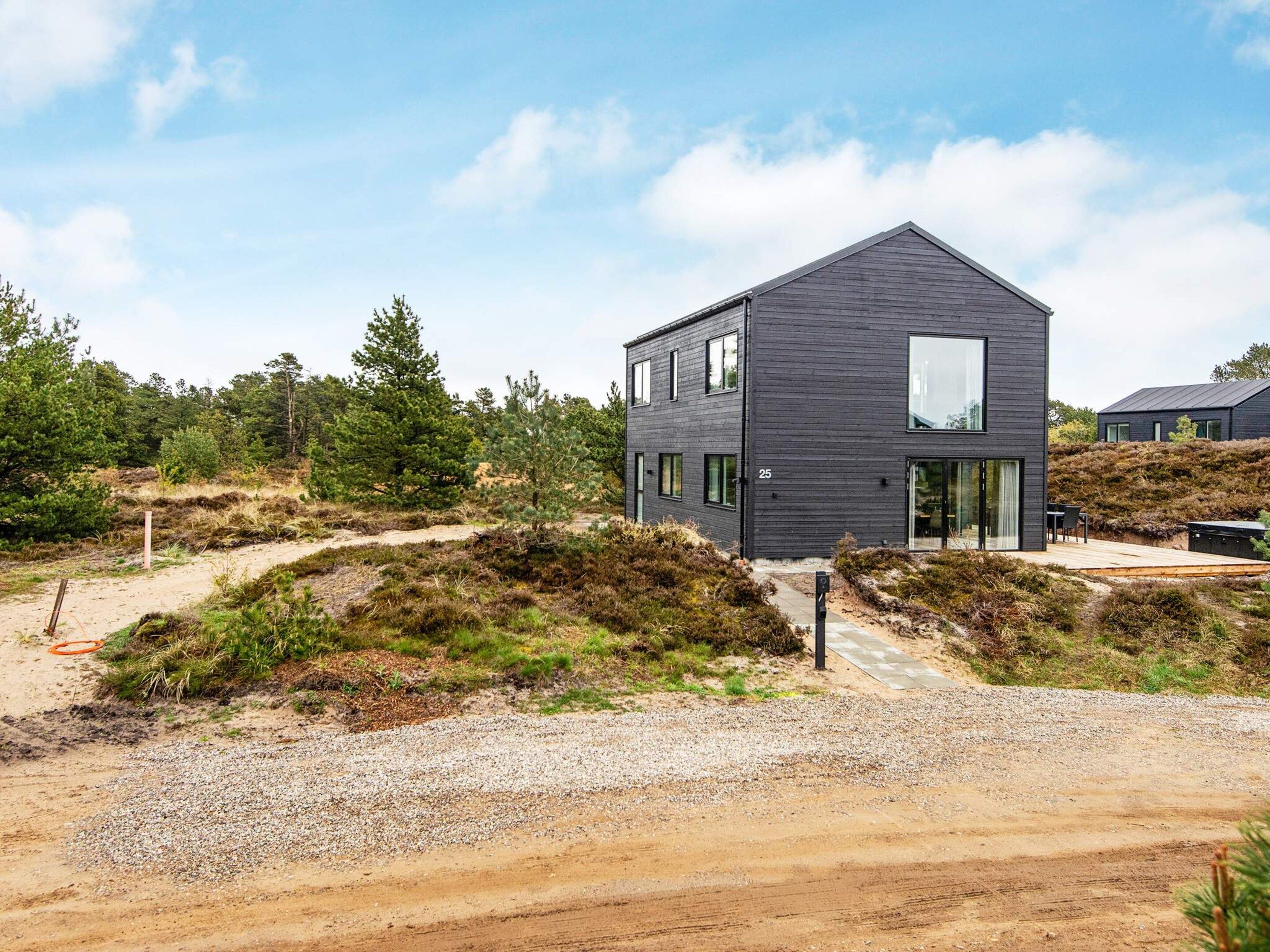 A modern two-story house with a dark exterior, a visible number '25', and a gravel driveway leading to a wooden deck.