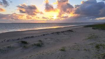 A beach with a sunset, sandy shore, and a clear sky.