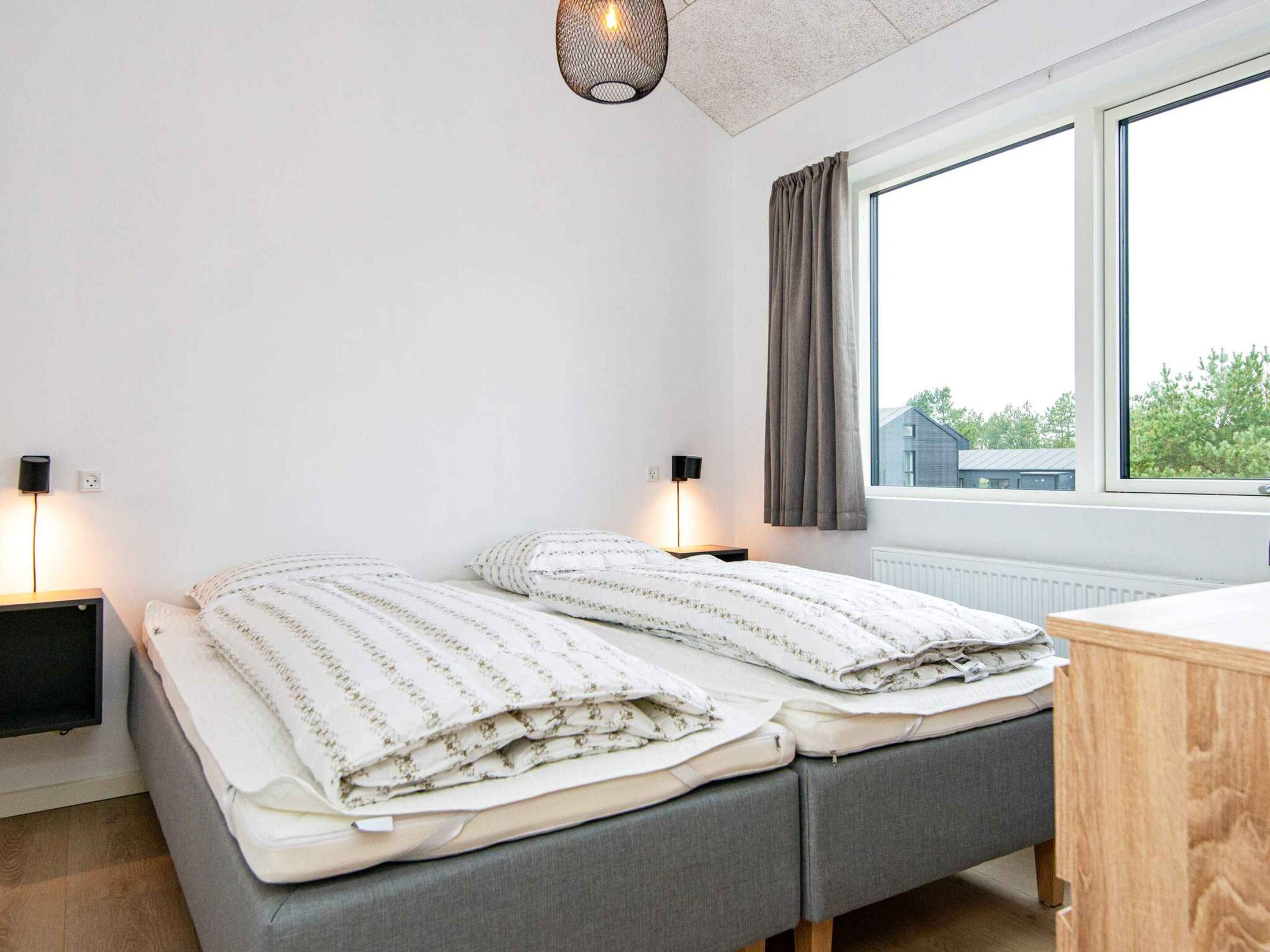 A bedroom with two beds, bedside lamps, a window with curtains, and a view of buildings outside.