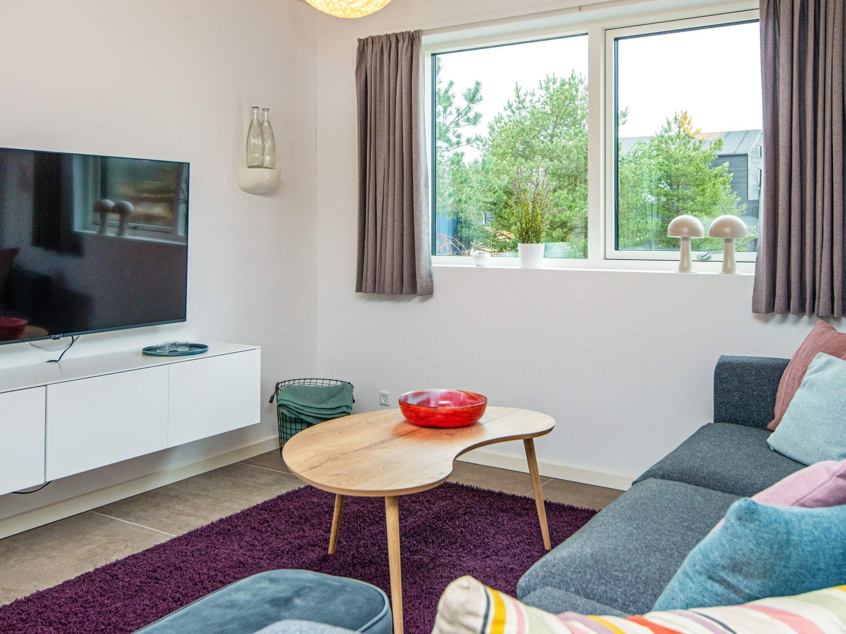 A modern living room with a flat-screen TV, a sofa, a coffee table, and a window with curtains.