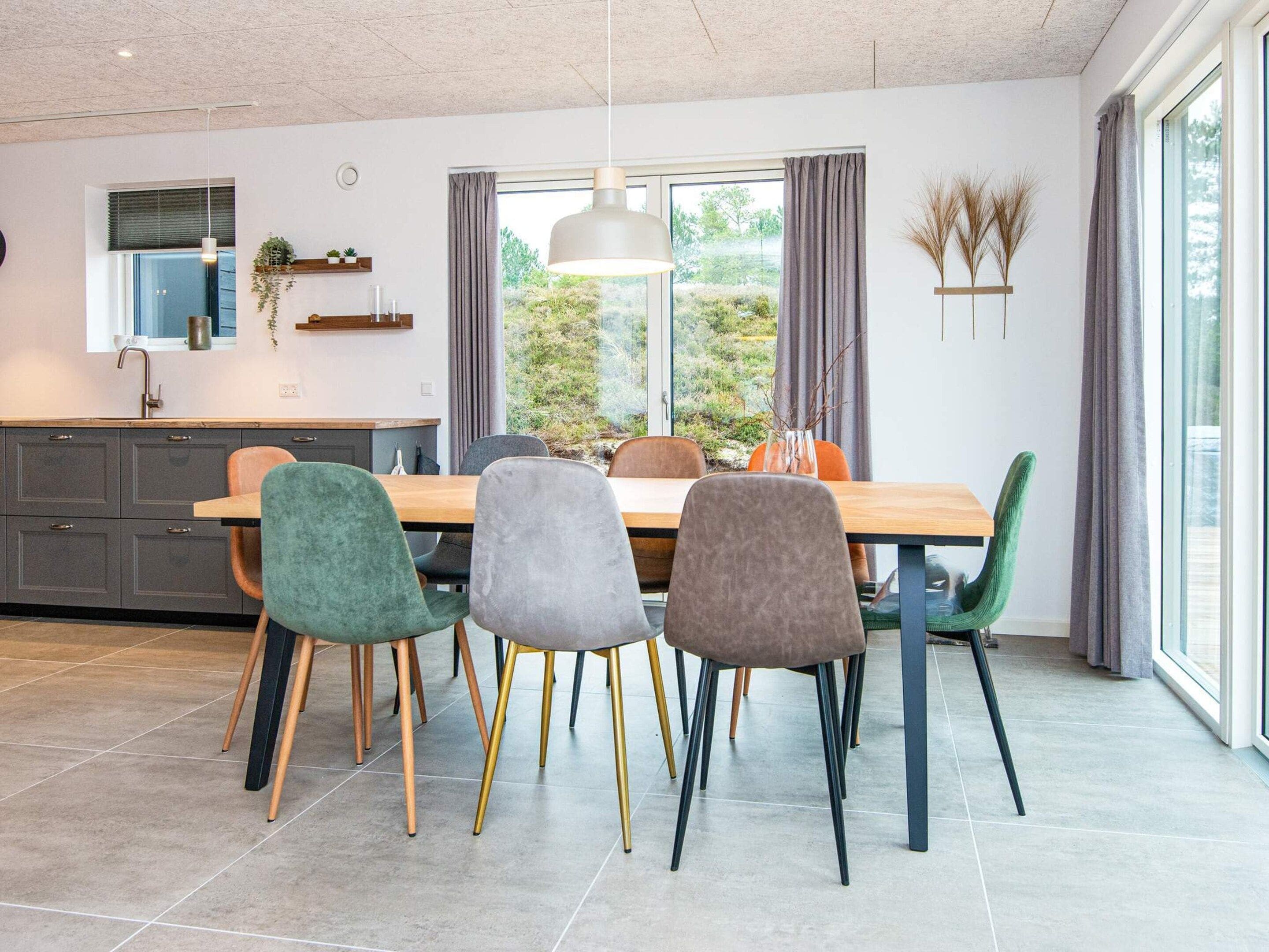 A modern kitchen with a dining area, featuring a large window, grey cabinets, and a wooden dining table with chairs.