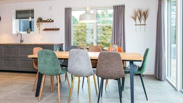 A modern kitchen with a dining area, featuring a large window, grey cabinets, and a wooden dining table with chairs.