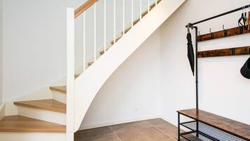 Eine Treppe mit Holzboden und weißen Geländern, eine Metallbank und ein an der Wand befestigter Hakenstreifen.