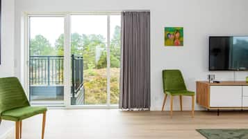 Ein modernes Wohnzimmer mit einer Schiebeglasdoor zum Balkon, ein mit Stoff bezogener grüner Sessel, ein Holzschrank und ein Flachbildfernseher.