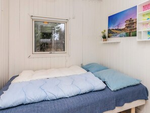 A bedroom with a single bed, a window, a wall-mounted shelf with a plant, and a wall art piece.