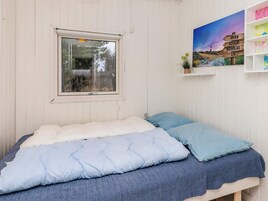 Un dormitorio con una cama individual, una ventana, un estante en la pared con una planta y una obra de arte.
