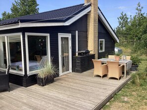 A modern house with a deck, a barbecue area, and outdoor furniture.