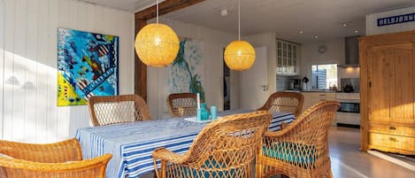 A dining area with wicker chairs, a striped tablecloth, and pendant lights.