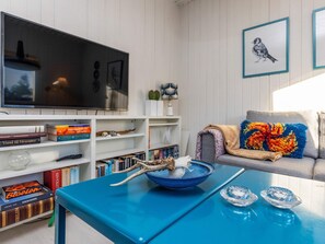 A living room with a television, bookshelves, a sofa with colorful cushions, and a blue coffee table.