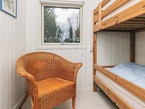 Una habitación con una cama litera, una silla de mimbre y una ventana que da a un paisaje de árboles.