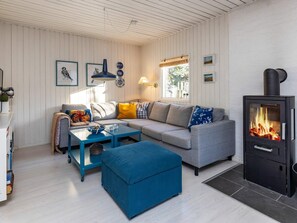 A cozy living room with a sofa, ottoman, and a black wood-burning stove.
