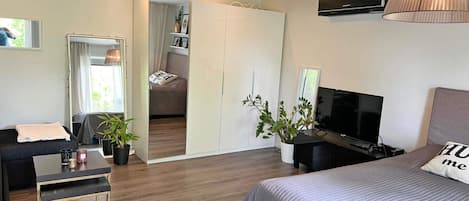 A modern bedroom with a bed, a TV, a desk, and a seating area.