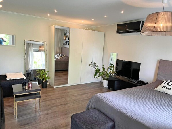 A modern bedroom with a bed, a TV, a desk, and a seating area.