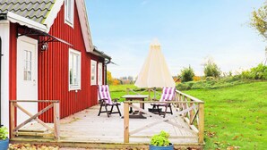 En röd byggnad med en träveranda, två stolar, ett bord och ett stort parasoll.