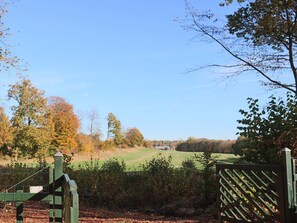 Een landelijk landschap met een houten poort, bomen en een grasveld.