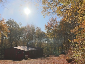 Eine Hütte, umgeben von Bäumen mit Herbstlaub, einem klaren Himmel und Sonnenschein.