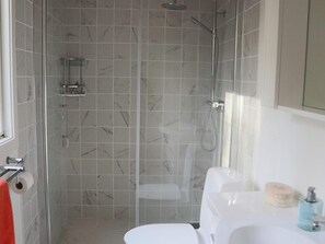 Une salle de bain avec une douche à parois de verre, des toilettes blanches et un lavabo équipé de produits de toilette.