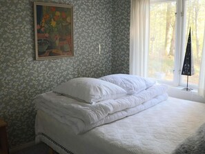 A neatly made bed with white bedding in a room with floral wallpaper and a painting on the wall.