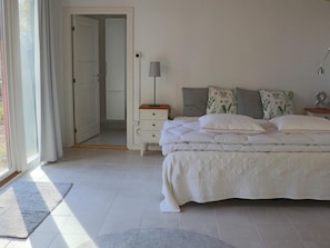 Ein Schlafzimmer mit einem Bett, Nachttischen, einer Lampe und einer Tür zu einem anderen Raum.