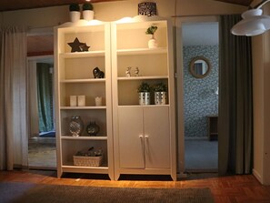 A room with a white cabinet with multiple shelves, a small plant on top, and a decorative sign.