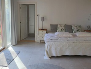 Une chambre à coucher avec un lit, des tables de chevet, une lampe et une porte donnant sur une autre pièce.