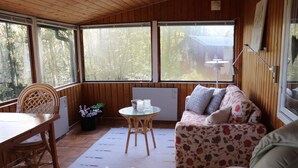 A cozy room with a wooden ceiling, a sofa with floral upholstery, a dining table with chairs, and a small table with a lamp. - 4 Person Holiday Home in Skanes-fagerhult (Skånes Fagerhult)