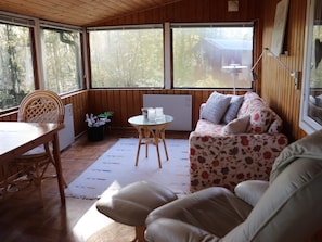 Ein gemütliches Zimmer mit Holzbalkendecke, einer Couch mit floralem Bezug, einem Esstisch mit Stühlen und einem kleinen Tisch mit einer Lampe.
